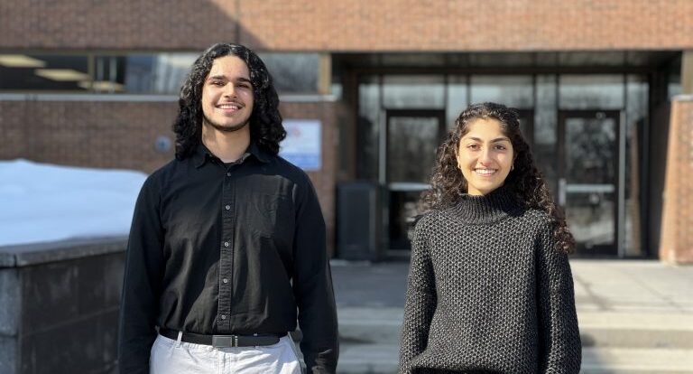 Two students pose in front of the college,